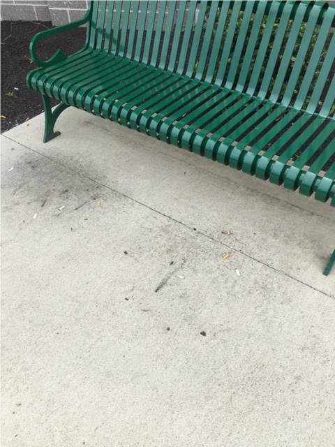 A bench outside a business with cigarette butts and other small trash littered across the ground.